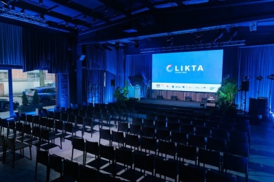 Konferences “LIKTA JAUDĀ 2025” norises vieta ar skatuvi un ekrānu, uz kura redzams LIKTA logo; zālē izvietotas skatītāju sēdvietas.