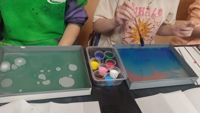 Skolēni ebru tehnikā glezno uz ūdens, izmantojot krāsas un otas meistarklases laikā