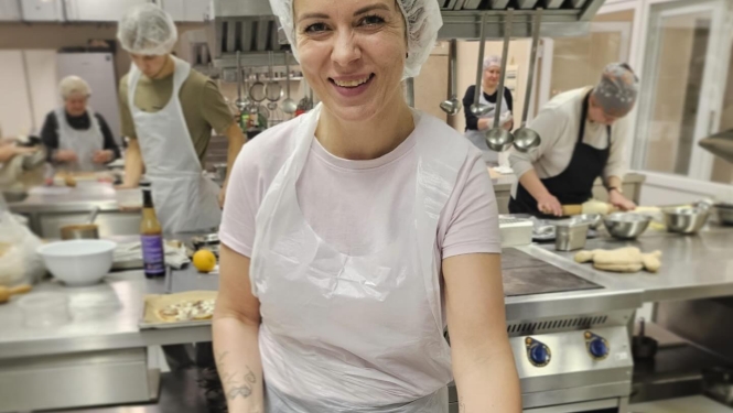 Neformālās izglītības kursa vadītāja pasniedz dalībniekiem svaigi ceptu picu, daloties ar profesionāliem padomiem ēdienu gatavošanā.