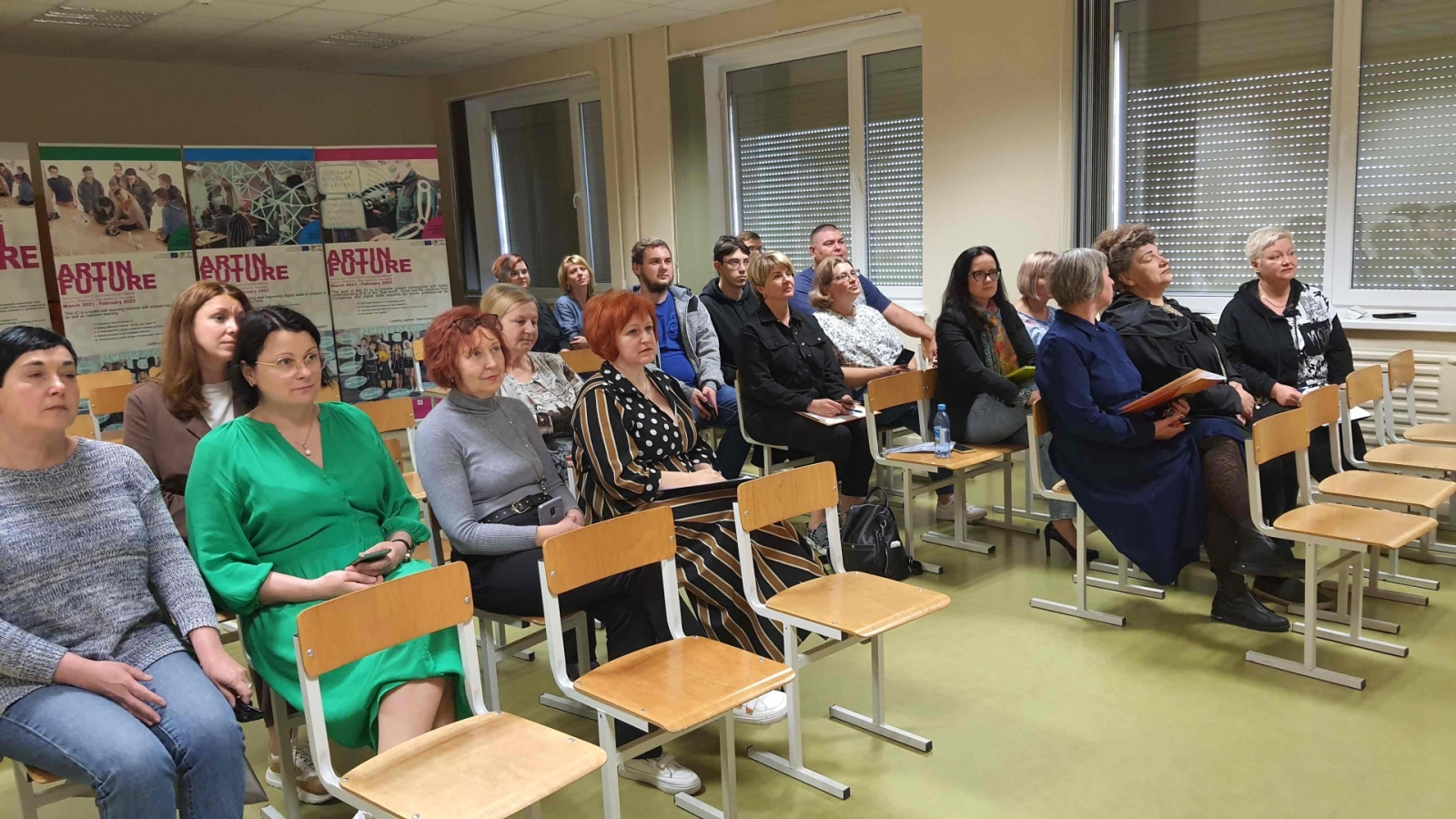 cilvēki sēž uz krēsliem un klausās prezentāciju