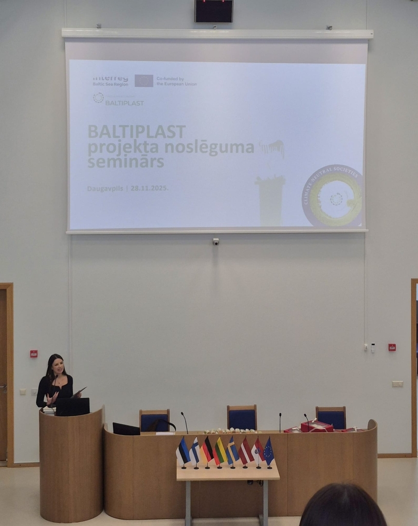 BALTIPLAST starptautiskā projekta noslēguma seminārs Daugavpilī – referente uzstājas auditorijā, fonā redzams prezentācijas ekrāns ar semināra nosaukumu un Eiropas Savienības līdzfinansējuma norādi (28.11.2025.).