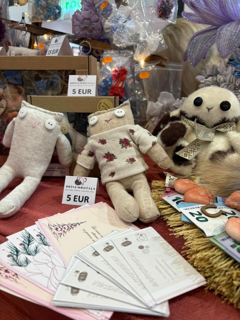 Skolēnu mācību uzņēmuma “Brīnumrotaļa” darinātās tekstila rotaļlietas un informatīvie materiāli uz tirdzniecības galda.