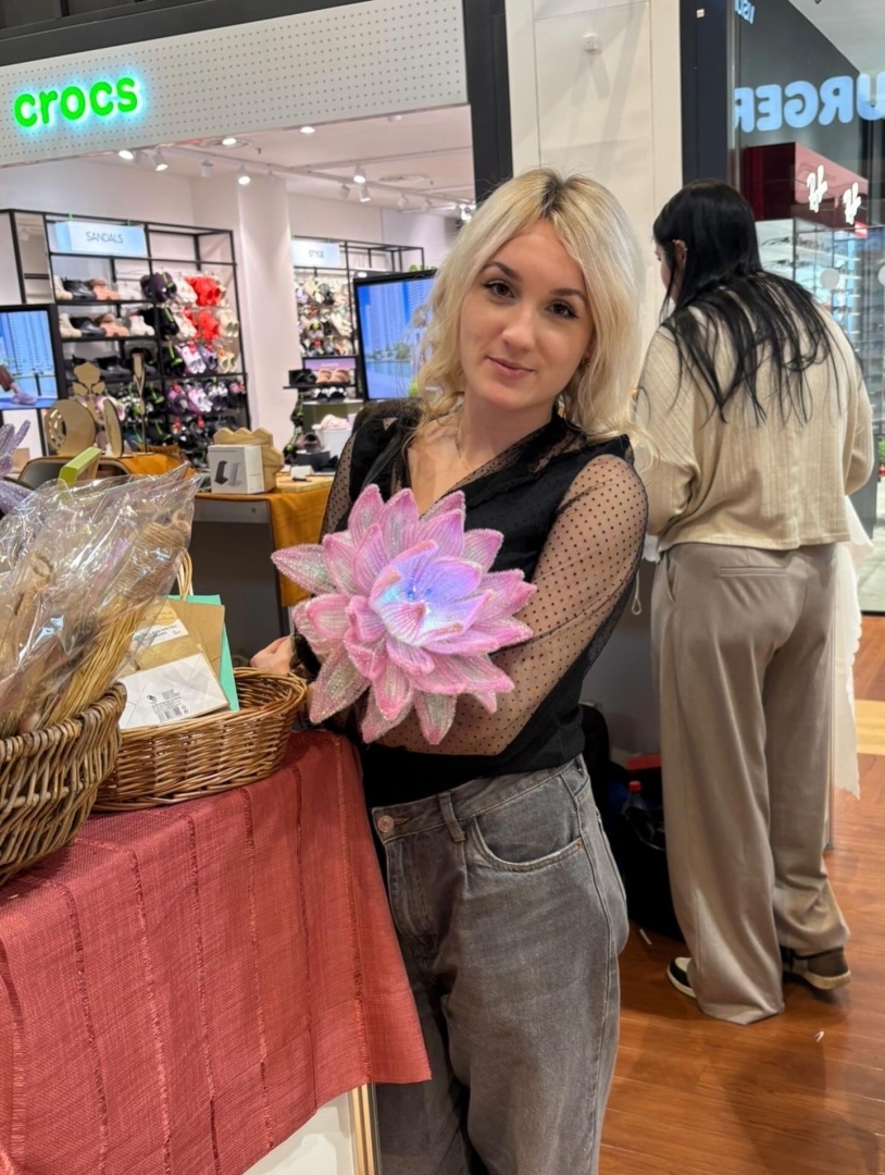 Skolēnu mācību uzņēmuma “Brīnumrotaļa” pārstāve demonstrē ar rokām veidotu dekoratīvu ziedu pasākumā “Cits Bazārs”.