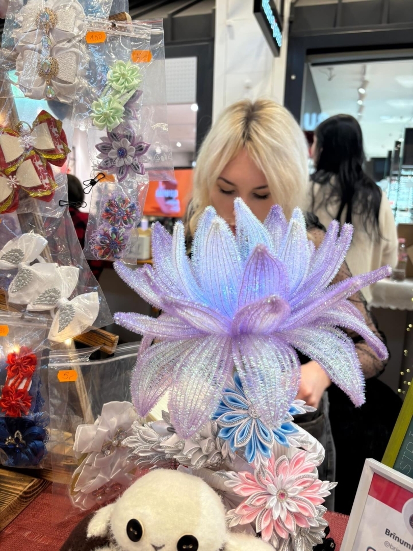 Detalizēts skats uz skolēnu mācību uzņēmuma “Brīnumrotaļa” dekoratīvajiem ziediem un rokdarbiem tirdzniecības stendā.