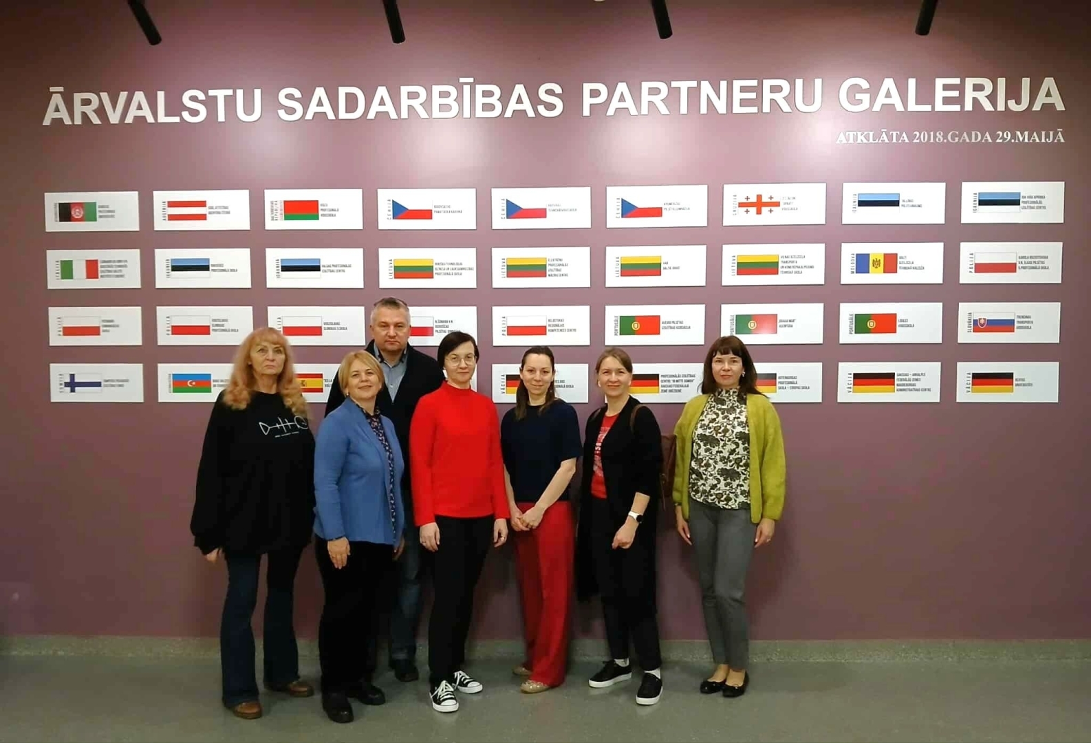Projekta dalībnieki pie ārvalstu sadarbības partneru galerijas ar valstu karogiem.