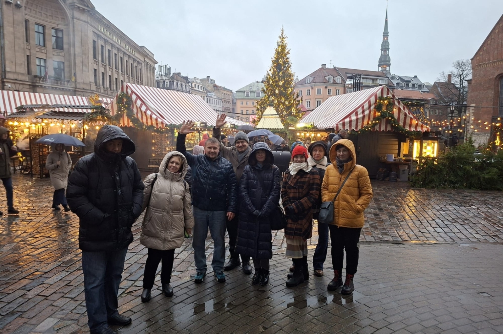 Projekta dalībnieku grupa Ziemassvētku tirdziņā Rīgā pie svētku eglītes.