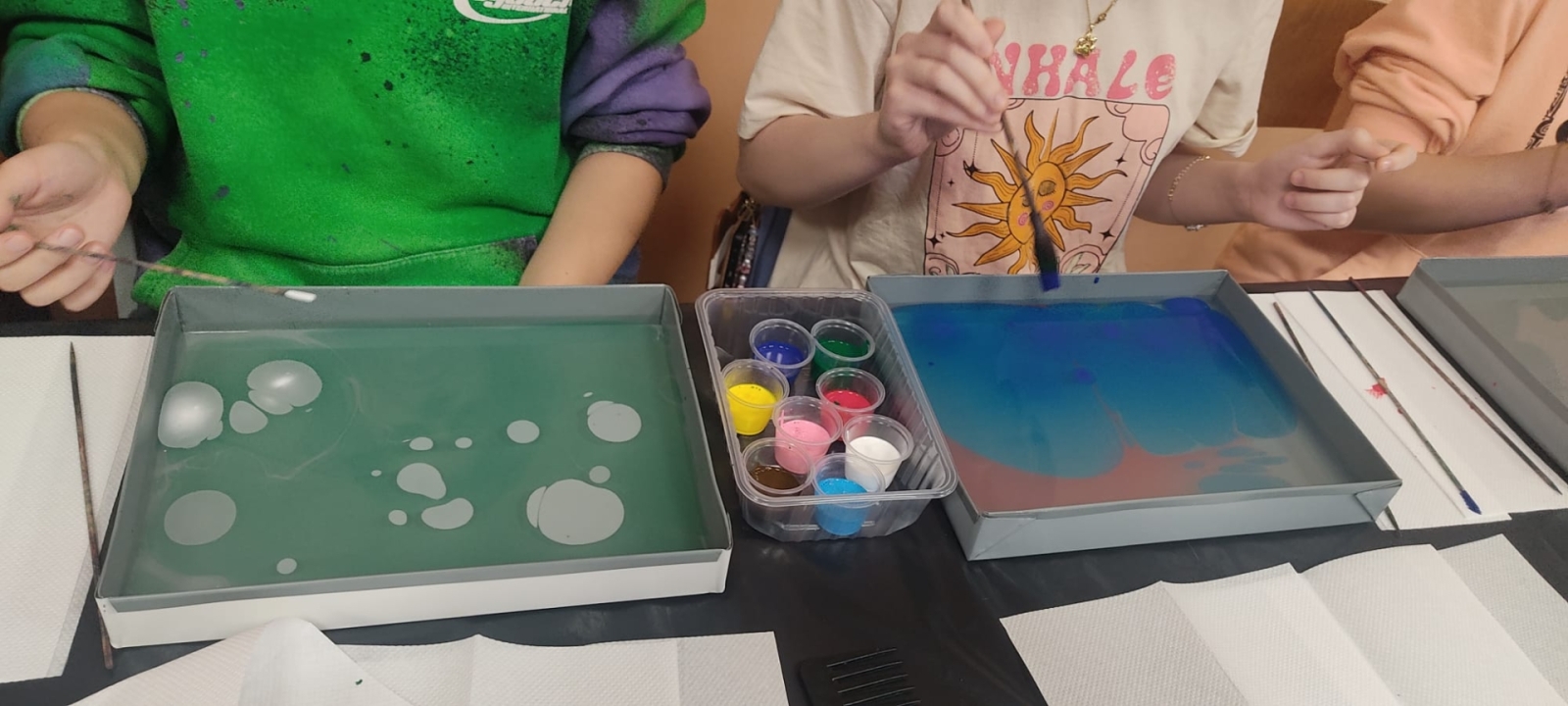 Skolēni ebru tehnikā glezno uz ūdens, izmantojot krāsas un otas meistarklases laikā