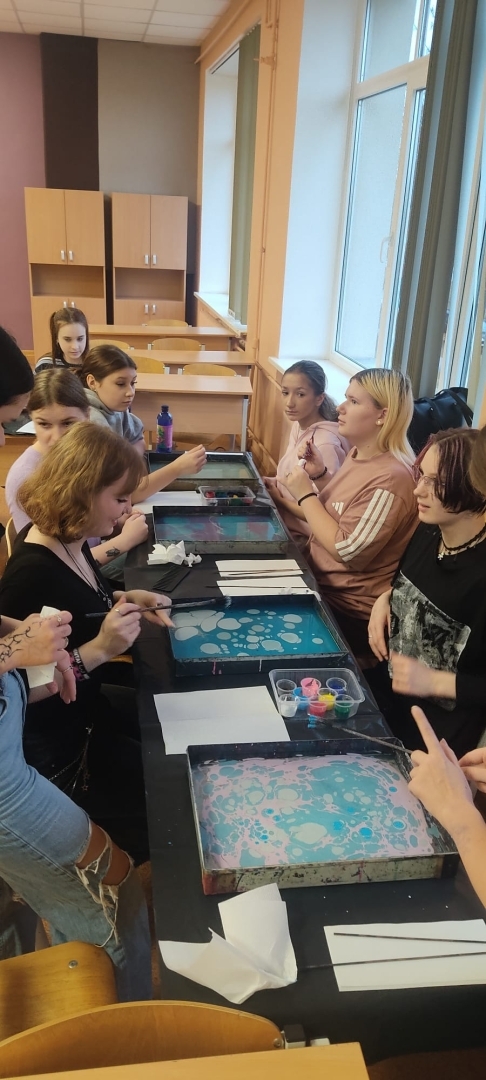 Skolēni klases telpā piedalās ebru meistarklasē un veido rakstus uz ūdens virsmas