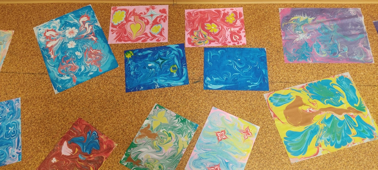 Skolēnu veidoto ebru darbu izstāde, izvietota uz grīdas, demonstrējot dažādus krāsu rakstus