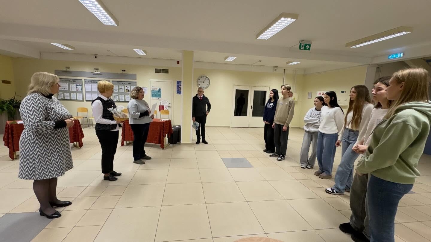 Plašs skats uz konkursa norisi – skolotāji un komisijas locekļi stāv pretī izglītojamajiem, kuri izkārtojušies rindā pasākuma telpā.