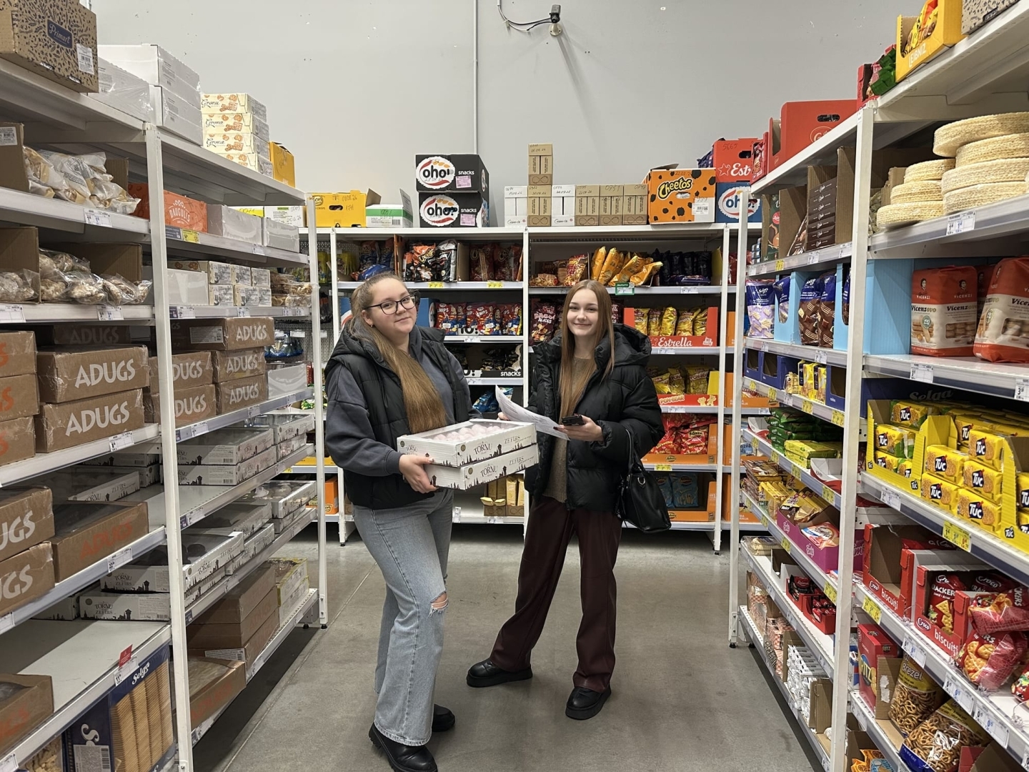 Izglītojamās veic uzdevumu pie saldētavu vitrīnām PROMO Cash&Carry veikalā