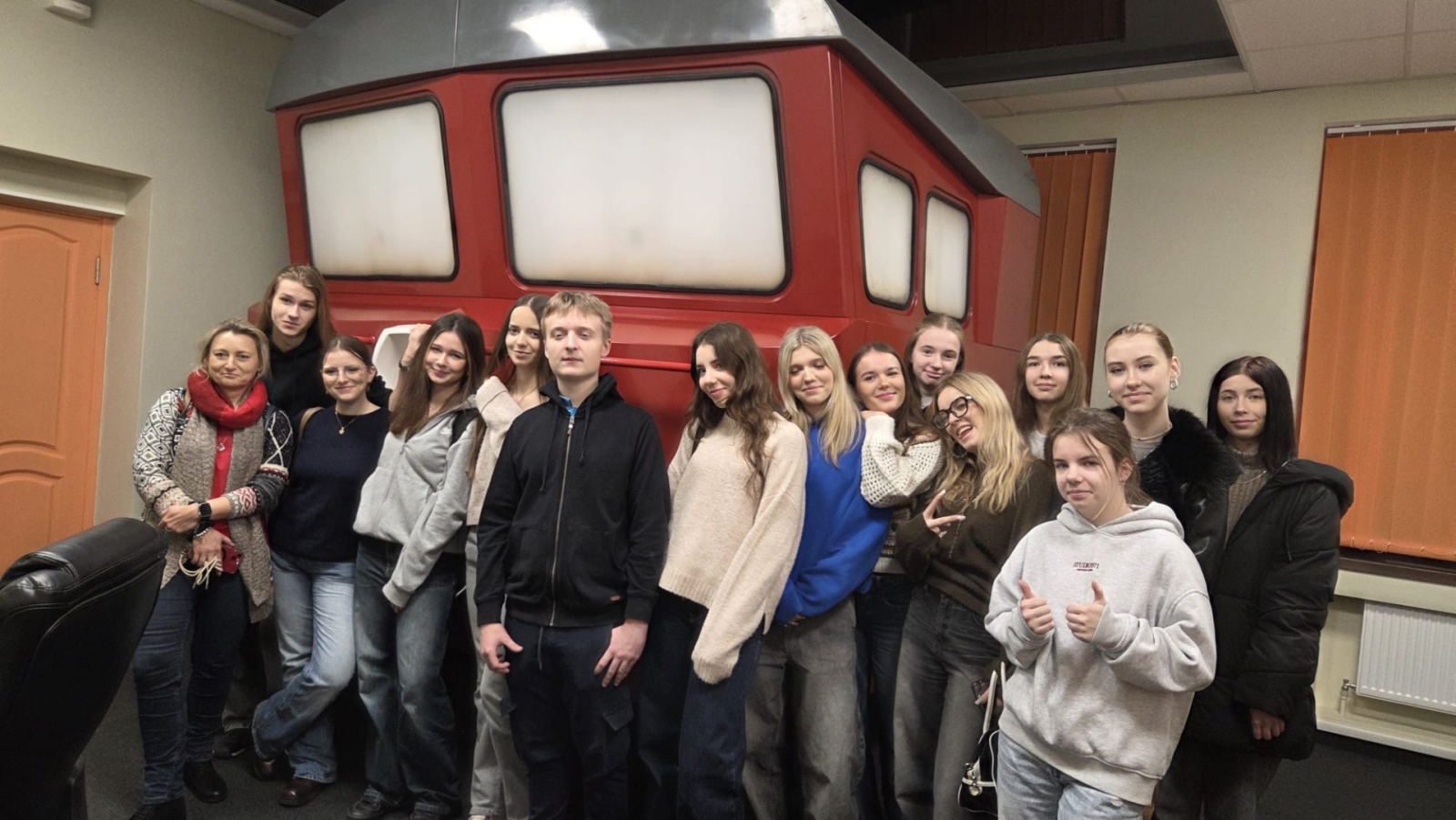 Latvijas un Polijas skolēni un skolotāji kopbildē tehnikuma pie lokomotīva simulatora