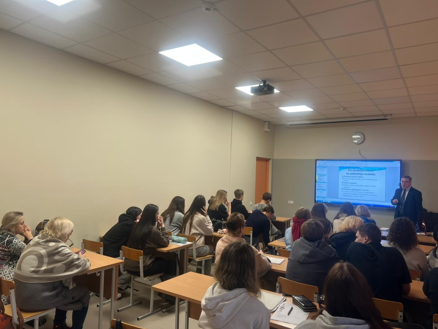 Mācību stunda ar vieslektoru tehnikumā, skolēni klausās prezentāciju auditorijā