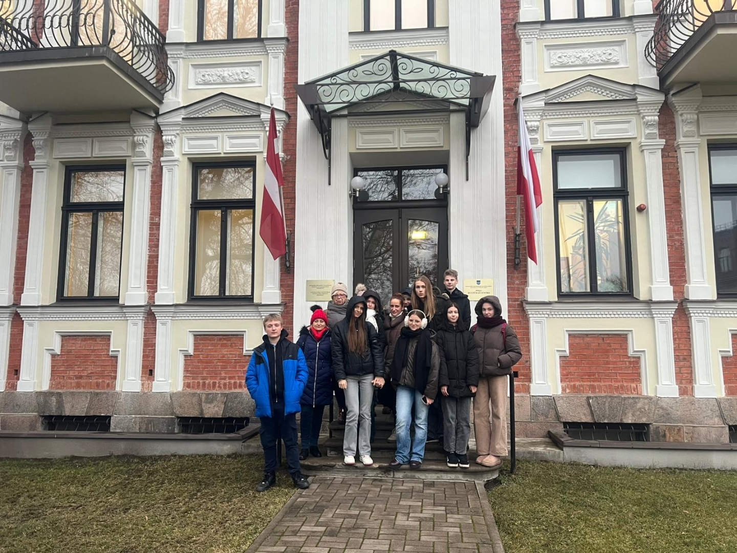 Latvijas un Polijas skolēni vakara pastaigā pilsētā pie svētku gaismas objektiemPolijas viesu kopbildē pie Daugavpils Poļu kultūras centra ēkas