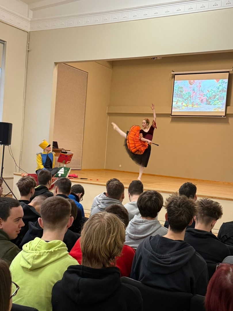 Baleta izrādes “Riekstkodis” aina ar dejotāju oranžā kostīmā un Riekstkoža tēlu uz skatuves.