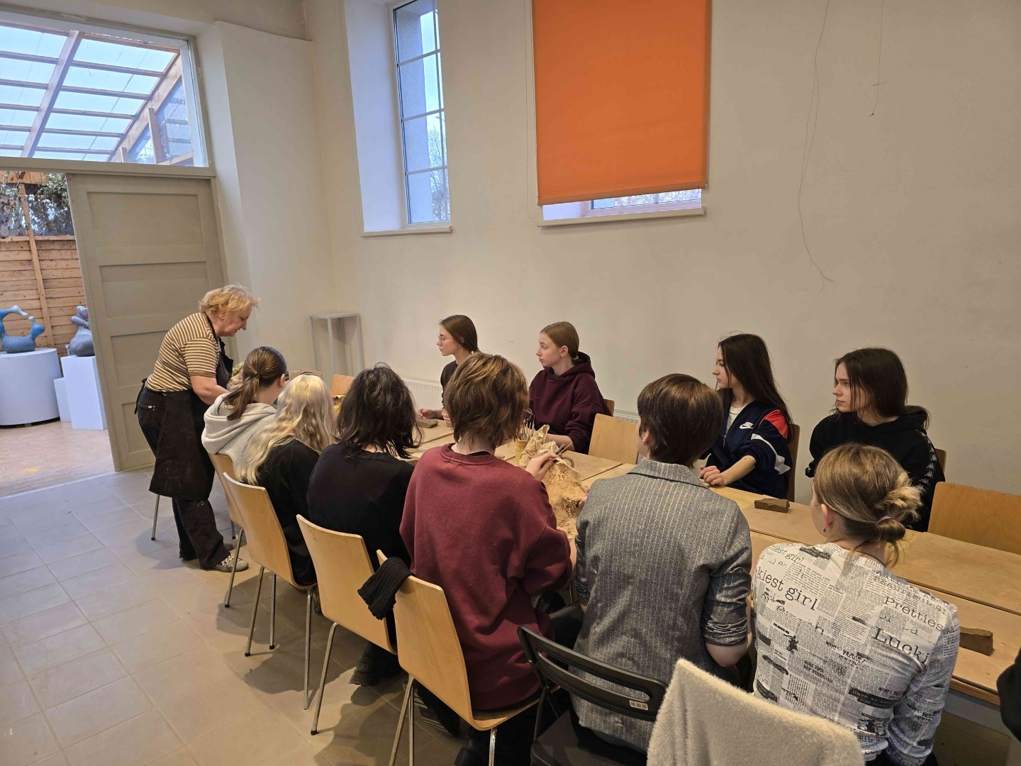 Grupas izglītojamie kopā ar nodarbības vadītāju strādā ar mālu pie galda muzejpedagoģiskās nodarbības laikā