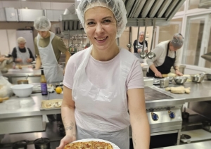 Neformālās izglītības kursa vadītāja pasniedz dalībniekiem svaigi ceptu picu, daloties ar profesionāliem padomiem ēdienu gatavošanā.