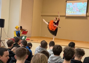 Baleta izrādes “Riekstkodis” aina ar dejotāju oranžā kostīmā un Riekstkoža tēlu uz skatuves.