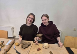 Divas izglītojamās smaida un demonstrē savus no māla veidotos darbus keramikas nodarbībā