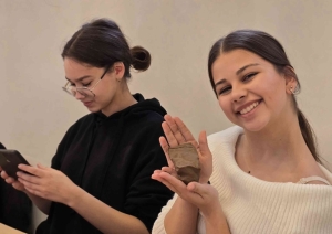 Izglītojamā rāda rokās turētu māla izstrādājumu, kamēr cita dalībniece strādā ar telefonu